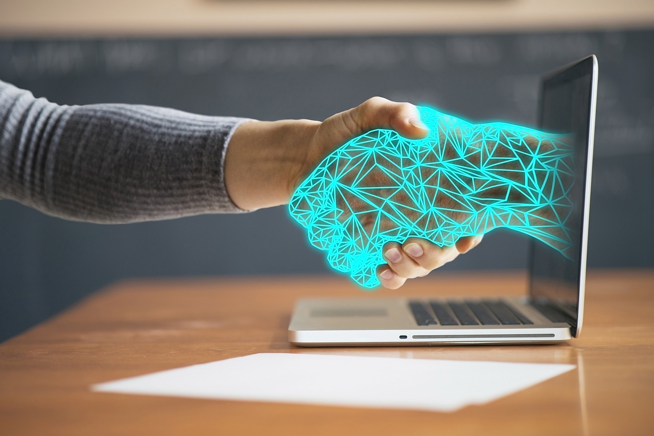 Image of a human shaking hands with an AI digital hand extending from a laptop