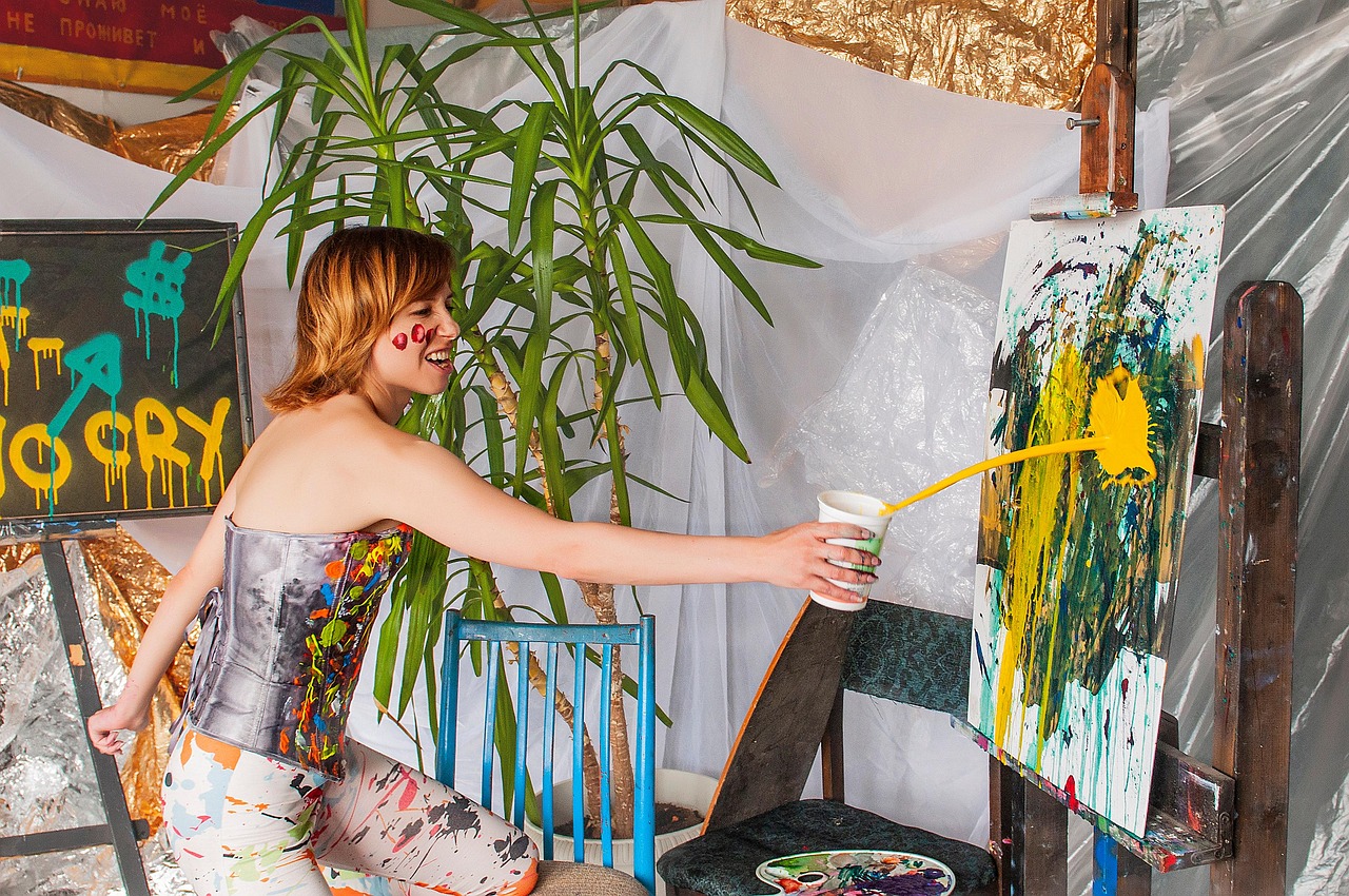 Creating an Online Art Portfolio | Woman smiling and tossing yellow paint onto a canvas